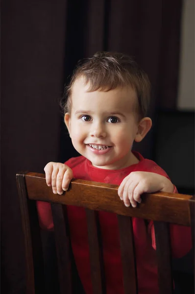 Mignon garçon de 2 ans dans une chemise rouge posant debout sur une chaise . — Photo