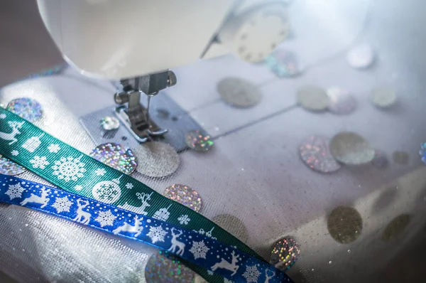 Glittering festive fabric in sewing machine and blue and green Christmas ribbons. Production of costumes for christmas holidays. — Stock Photo, Image