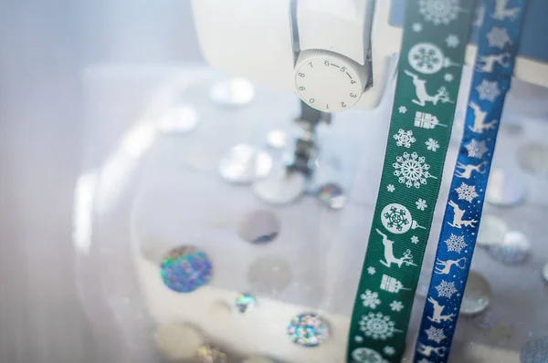 Glittering festive fabric in sewing machine and blue and green Christmas ribbons. Production of costumes for christmas holidays. — Stock Photo, Image