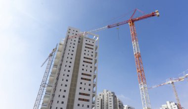 İsrail 'in Birüssebi kentsel manzarasında, sisli bir sabahta modern yerleşim binaları, yeşil bir şehir parkı, ağaçlar, su yansıması ve çağdaş mimari yer alıyor..