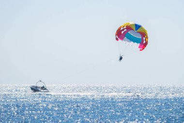 Parasailing denizde. Küçük bir motorlu tekne birkaç kişiyle renkli bir paraşüt kullanıyor. Seçici odaklanma. Yatay yönelim.