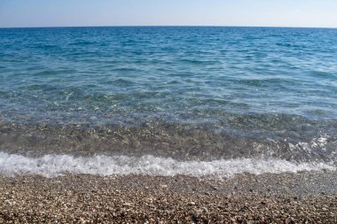 Mavi deniz suyu çakıl taşlı bir plajda sıçrıyor. Sahilden görüntü. Akdeniz 'de. Yatay görünüm.