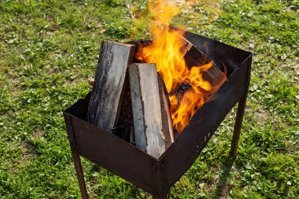 Wood-fired grill staying on the grass with a fire and burning wood in it. Horizontal orientation.