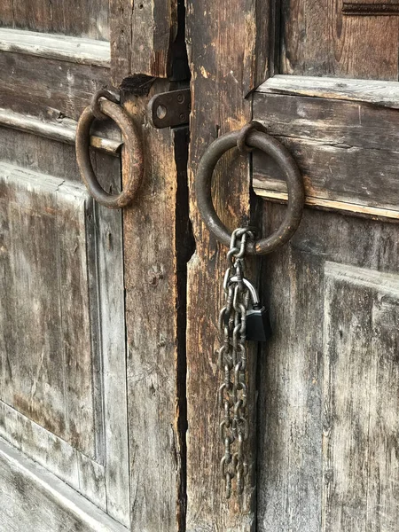 Yuvarlak metal kapı kolları ve kilidi olan asılı zinciri olan antik ahşap kapılar. Dikey yönelim.