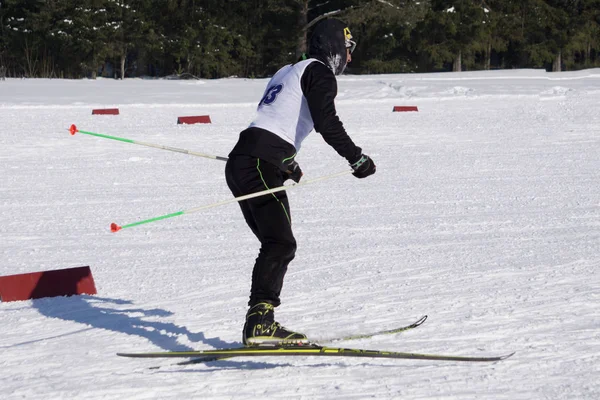 バックパックと黒い服で男性スキーヤーがスキーのバレーと素晴らしい青空で雪に覆われた丘を背景に雪の山の上からダウンします — ストック写真