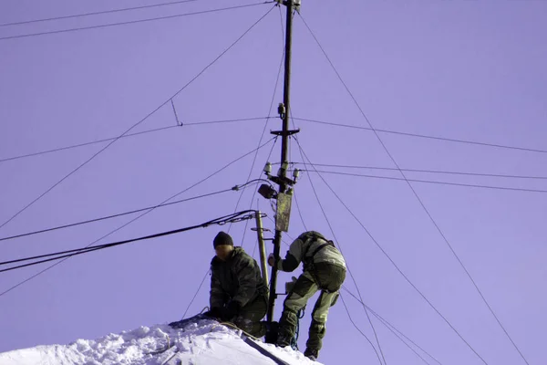 Equipo de trabajadores masculinos limpia el techo de la construcción de la nieve con palas en la seguridad de cinturones de mantra . — Foto de Stock