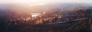Panorama view of autumn colored forest from air at sunset with lake water reflecting and an empty road, Finland clipart
