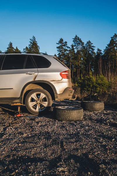 Changing of tire on a gravel field with a jack, with studded winter tires laying on the ground