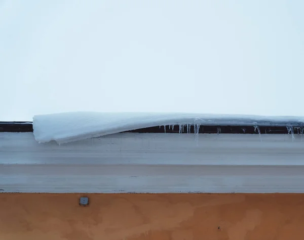 Snow starting to melt on the roof of a building and hanging over the roof line — Stock Photo, Image