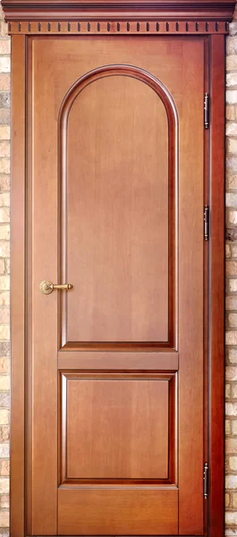 Wooden interroom carved door in a door frame made of maple tree with brass handle with geometric ornaments on brick background