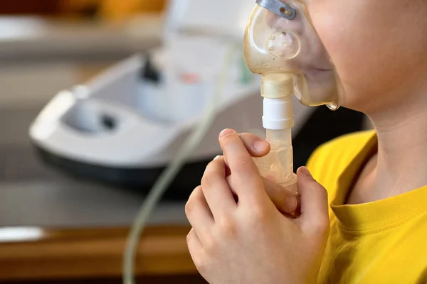 Child makes inhalation at home with nebulizer on out of focus ba