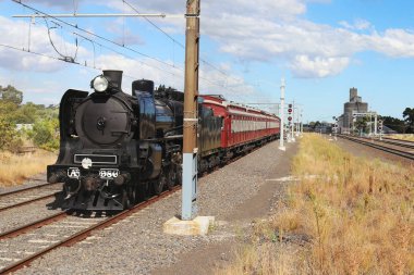 an A-class steam engine hauling red rattler carriages at Sunshine railway station in Australia clipart