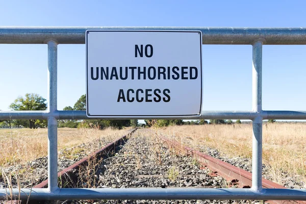 Een zwart-wit geen ongeoorloofde toegang waarschuwingsteken op het hek van een niet-afgesloten spoorlijn — Stockfoto