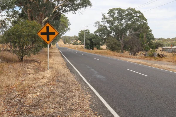 Señal amarilla con cruz negra que indica Encrucijada por delante en una carretera de campo — Foto de Stock