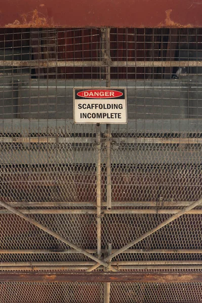 a red, black and white Danger, Scaffolding Incomplete warning sign at a maintenance work site