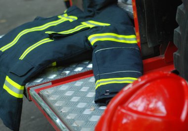 İtfaiyeci ceketi ve kaskı, itfaiye arabasının arkasında.