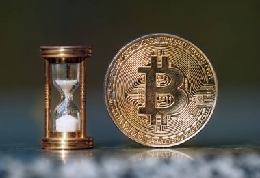 Fiziksel bitcoin ve kum saati zamanın geçtiğini gösteriyor.
