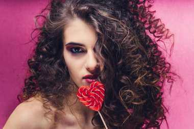 Güzel kızla kıvırcık: pembe bir arka plan üzerinde kırmızı kalp lolipop