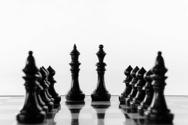Black chess king and queen stand on a chessboard between rows of pawns and bishops