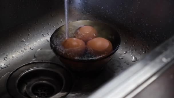 Tekoucí studená voda z vodovodního kohoutku na vařené kuřecí vejce — Stock video