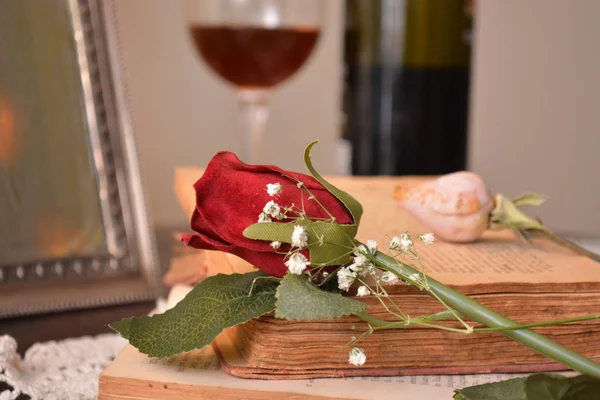 red rose flower on the books and glass red wine in background