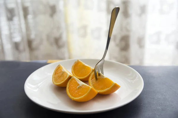 Orange cut in to slices on the white plate  with fork