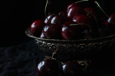 Siyah arka planda, kırsal tabakta taze, olgun kirazlar. Kapat..