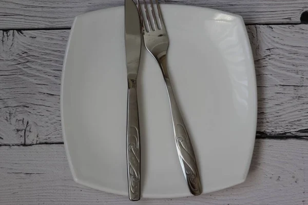 Empty plate, fork and knife over wooden background. Clean plate and cutlery on light background. Top view. Flat lay.