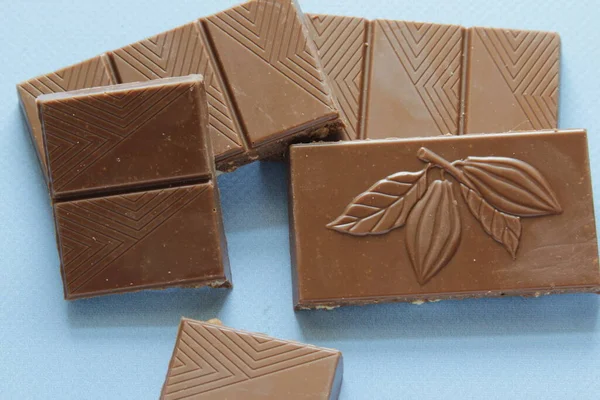 Milk chocolate pieces isolated on blue background from top view. Close up a chocolate bar isolated on blue background.