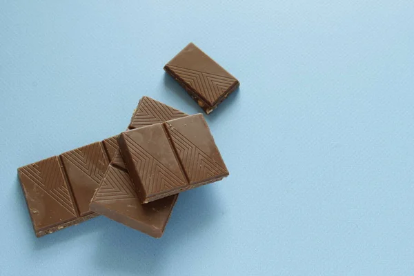 Piese de ciocolată cu lapte izolate pe fundal albastru din partea de sus. Închideți un bar de ciocolată izolat pe fundal albastru . — Fotografie, imagine de stoc