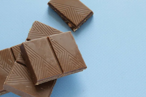Части молочного шоколада изолированы на синем фоне от верхнего вида. Закрыть плитку шоколада на синем фоне. — стоковое фото