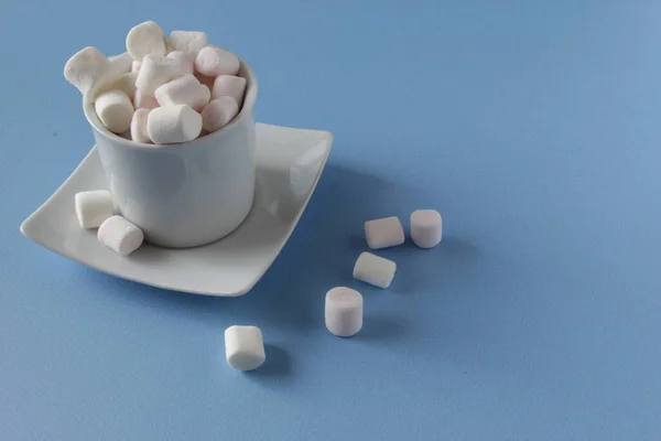 Branco Fluffy marshmallows em copo branco isolado no fundo azul. Mini marshmallows. Inverno conceito de fundo alimentar . — Fotografia de Stock