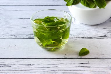 Ahşap arka planda taze nane çayı konsepti. Şeffaf bir fincanda nane çayı ve masada bir nane yaprağı.