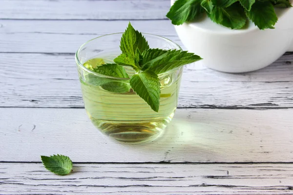 Fresh mint tea concept on a wooden background. Mint tea in a transparent cup and one mint leaf on the table