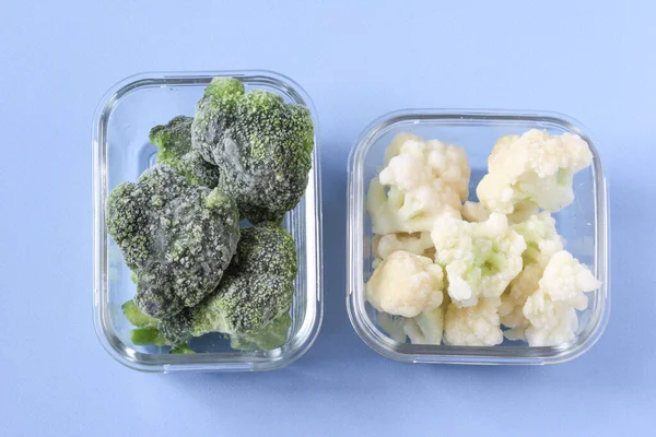 Verduras congeladas como la coliflor y la col de brócoli en los cuencos transparentes sobre el fondo azul de hormigón. Copiar espacio, vista superior — Foto de Stock