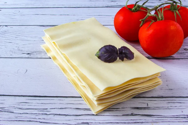 Lasagne blättert Nudeln mit Tomaten und Basilikumblättern auf einem hölzernen Hintergrund. Zutaten für ein italienisches Rezept. Kopierraum. — Stockfoto