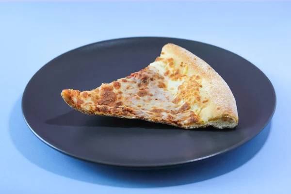 Rebanada seca de pizza sobre una mesa negra sobre un fondo azul. Concepto alimenticio. —  Fotos de Stock