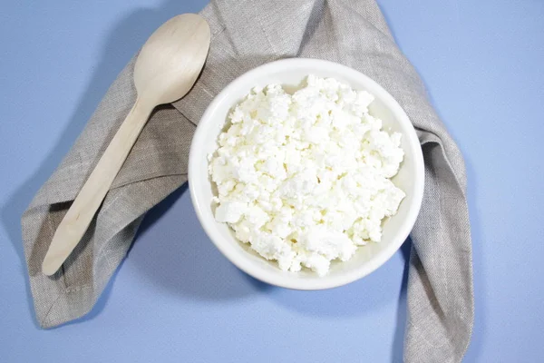 Cottage cheese in white bowl on blue table with spoon and napkin. Top view. Horizontal orientation.