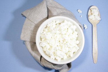 Beyaz kasedeki süzme peynir mavi masada kaşık ve peçeteyle. Üst Manzara. Yatay yönelim.