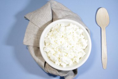 Beyaz kasedeki süzme peynir mavi masada kaşık ve peçeteyle. Üst Manzara. Yatay yönelim.