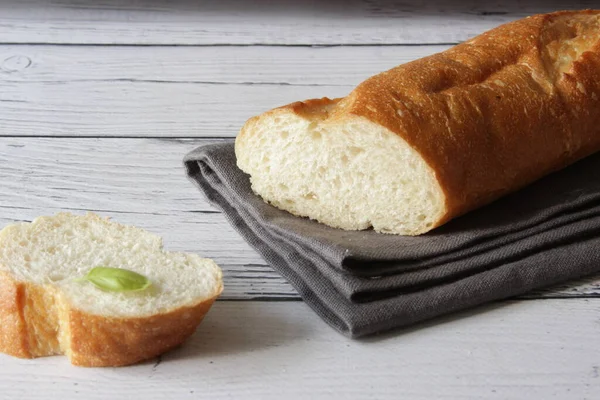 Baguette francesa de pan blando fresco sobre servilleta y fondo de madera. Hay varias piezas cortadas una al lado de la otra.. — Foto de Stock