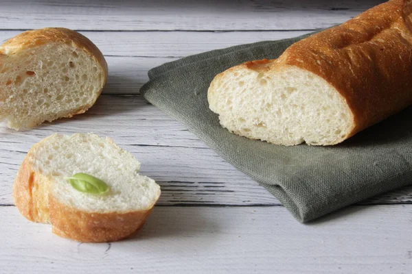 Baguette francesa de pan blando fresco sobre servilleta y fondo de madera. Hay varias piezas cortadas una al lado de la otra.. — Foto de Stock