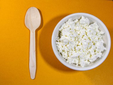 Turuncu masada beyaz kasede kaşık ile süzme peynir. Üst Manzara. Yatay yönelim.