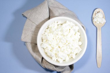 Beyaz kasedeki süzme peynir mavi masada kaşık ve peçeteyle. Üst Manzara. Yatay yönelim.