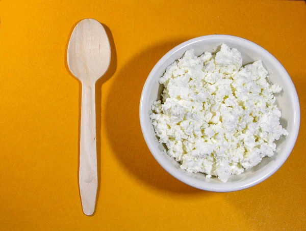 Turuncu masada beyaz kasede kaşık ile süzme peynir. Üst Manzara. Yatay yönelim.