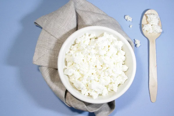 Beyaz kasedeki süzme peynir mavi masada kaşık ve peçeteyle. Üst Manzara. Yatay yönelim.