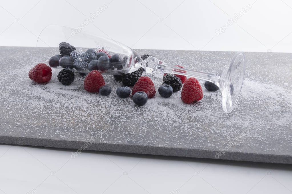 Fresh berries and a glass on a plate of granite whith sugar on a white background.  - Imagen
