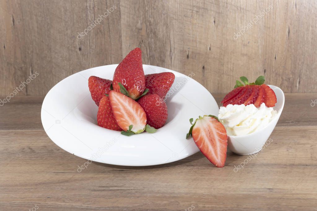 strawberries and whipped cream  on a white dish on a wooden background.  - Imagen