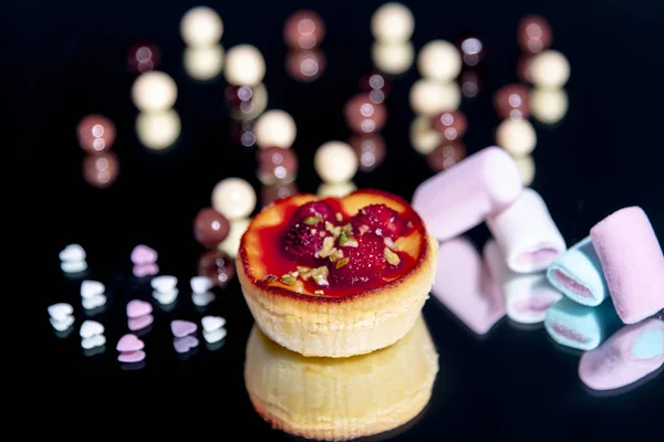 cheese cake with red fruit and marshmallow on a mirror and a black background with bokeh effect