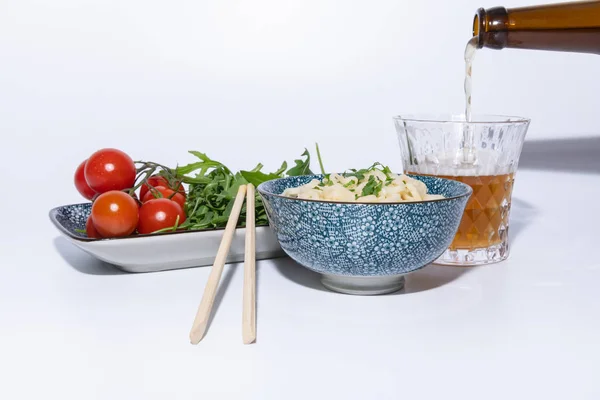 Nudlar i en skål med fräsch sallad, en öl och ätpinnar. Vit bakgrund — Stockfoto